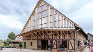 Das Foto zeigt eine Fachwerkscheune mit Satteldach. Der Giebel ist mit einer Konstruktion aus Holz und Glas versehen, die in ein Vordach übergeht. Kachel Vorschau