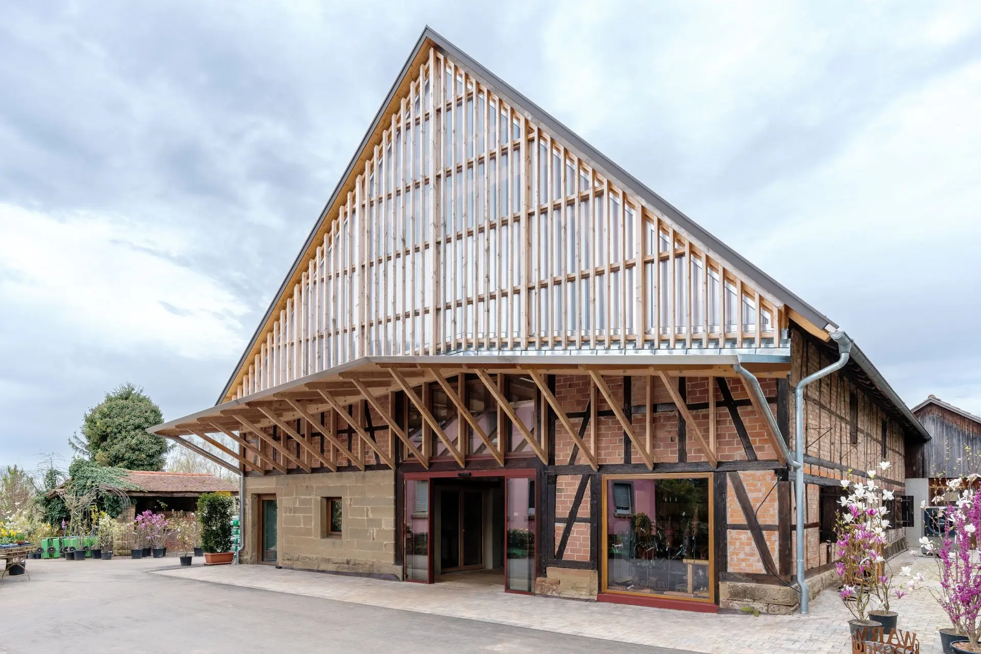 Das Foto zeigt eine Fachwerkscheune mit Satteldach. Der Giebel ist mit einer Konstruktion aus Holz und Glas versehen, die in ein Vordach übergeht.