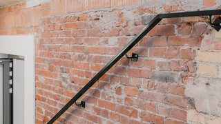 Man sieht eine Wand in einem Treppenhaus, sie ist unverputzt und besteht aus einem Mix von alten und neuen Ziegeln in verschiedenen Formaten und Farben.