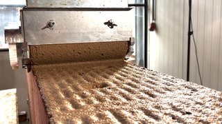 Auf dem Foto ist zu sehen, wie ein brauner Mörtel mit einer Mörtelrolle auf eine Mauerwerkswand aufgetragen wird. Kachel Vorschau