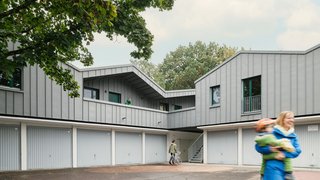 Auf einer L-förmigen Garagenanlage ist ein einstöckiger Aufbau, der mit grauem Titanzink verkleidet ist. Über eine außenliegende Treppe gelangt man nach oben. Kachel Vorschau