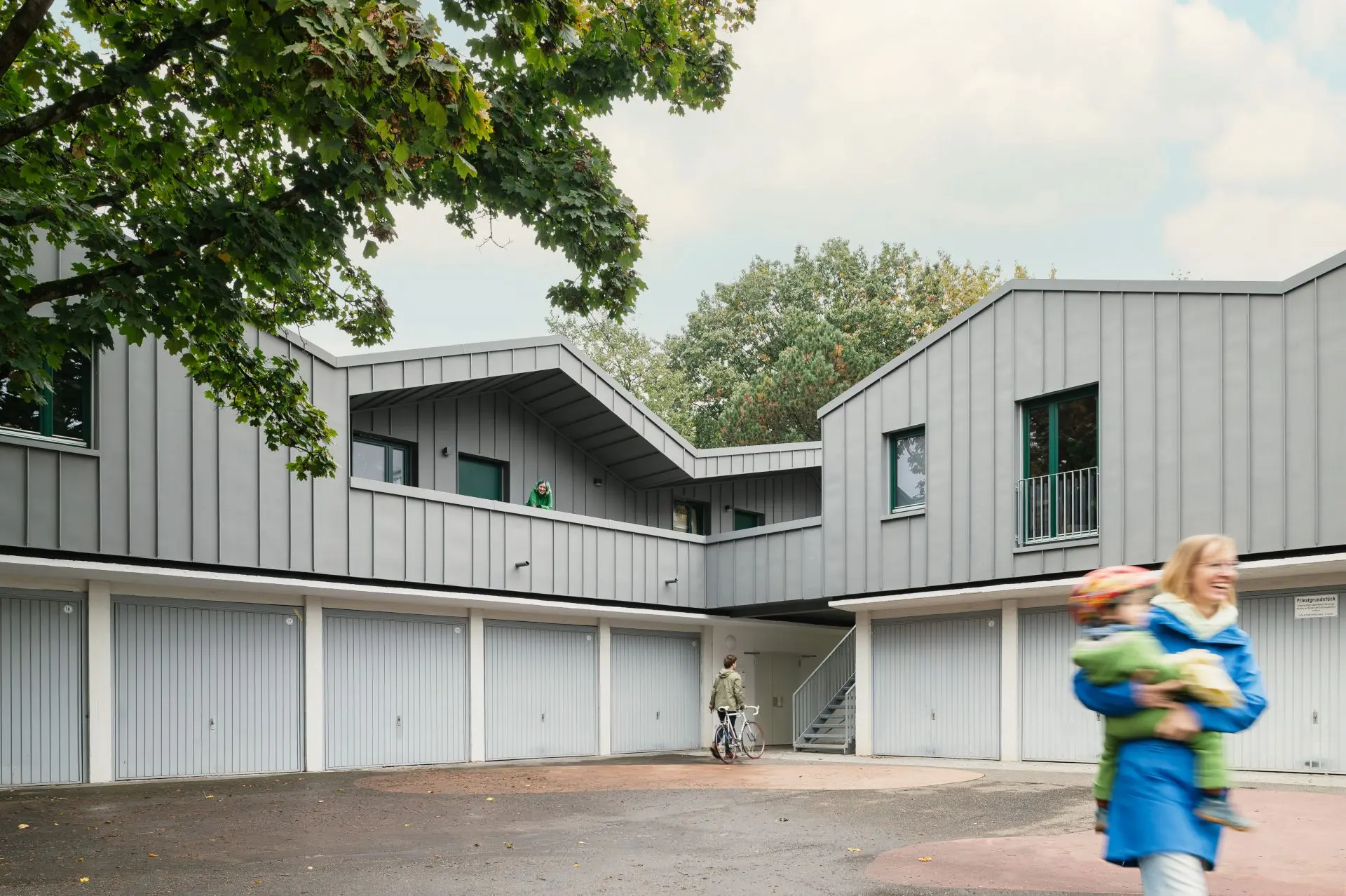Auf einer L-förmigen Garagenanlage ist ein einstöckiger Aufbau, der mit grauem Titanzink verkleidet ist. Über eine außenliegende Treppe gelangt man nach oben.