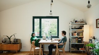 Zwei Personen sitzen an einem Tisch in einem hellen Raum mit Dachschrägen. Kachel Vorschau