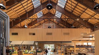 Das Foto zeigt den Innenraum der Markthalle mit Verkaufsständen aus hellem Holz. Das Satteldach der Halle ist durchzogen von Fensterbändern aus Solarglas. Kachel Vorschau
