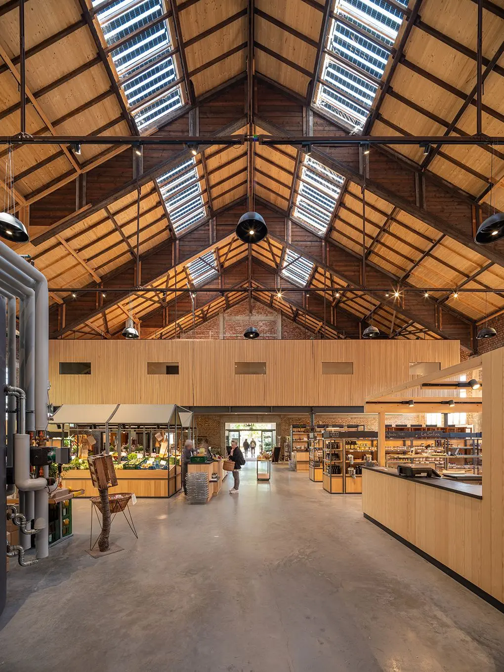 Das Foto zeigt den Innenraum der Markthalle mit Verkaufsständen aus hellem Holz. Das Satteldach der Halle ist durchzogen von Fensterbändern aus Solarglas.