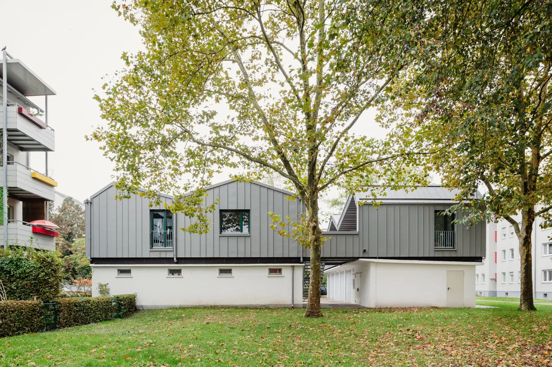 Die Aufstockung der Garagenanlage liegt zwischen Mehrfamilienhäusern in einer grünen Umgebung mit Bäumen.