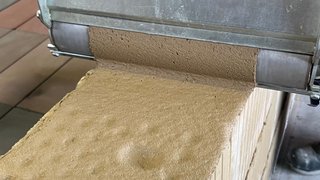 Auf dem Foto ist zu sehen, wie ein brauner Mörtel mit einer Mörtelrolle auf eine Mauerwerkswand aufgetragen wird. Kachel Vorschau